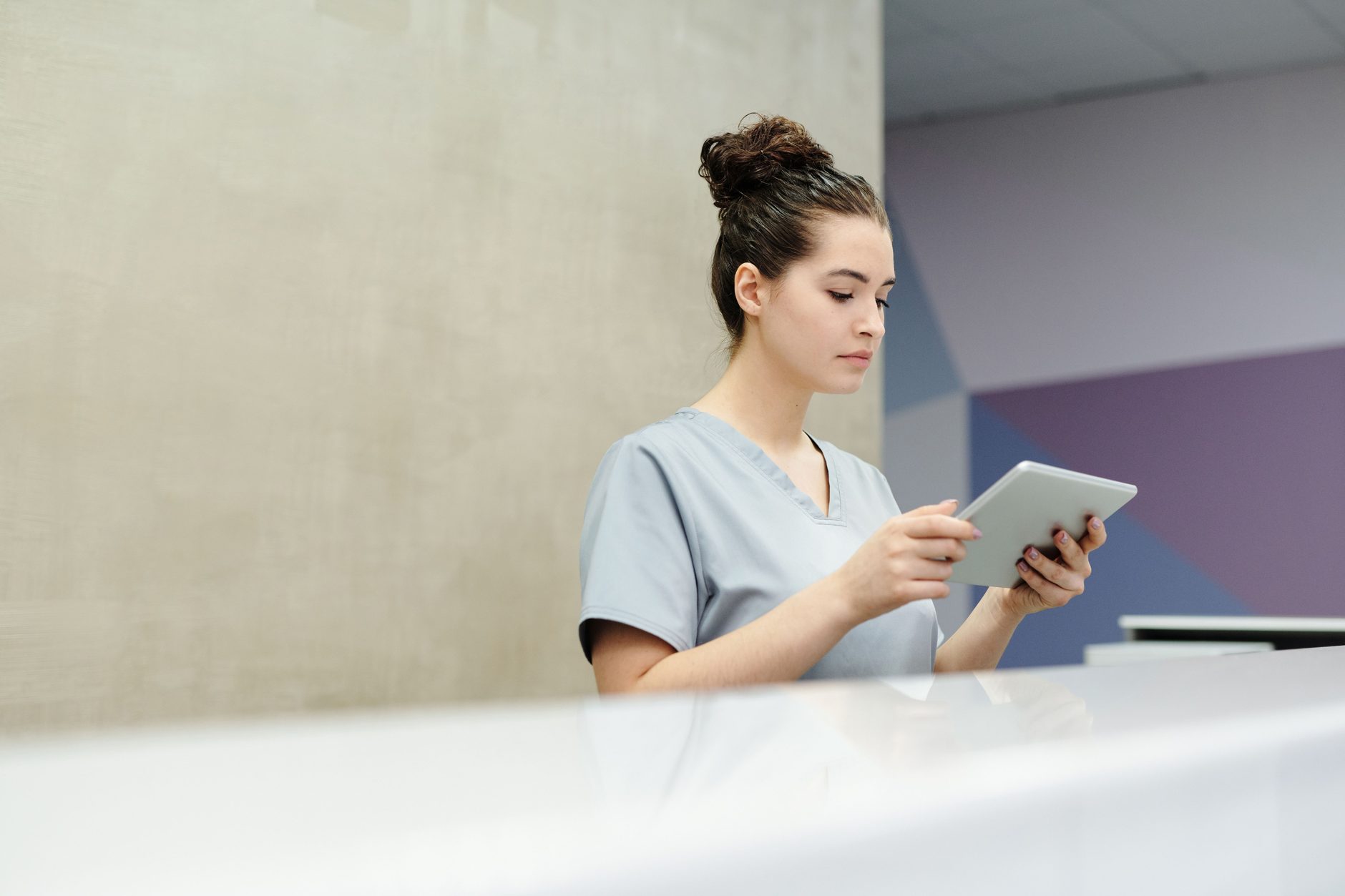 Empfangsmitarbeiterin in Praxiskleidung mit Tablet am Empfangstresen einer Arztpraxis.