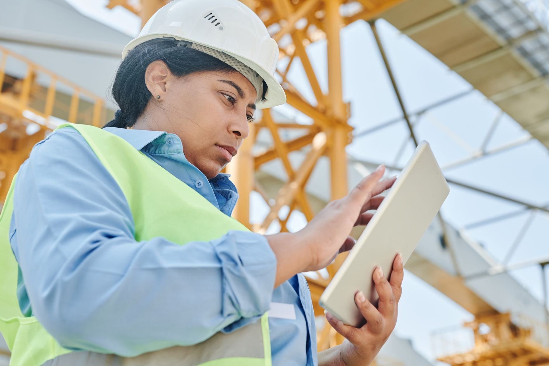A female engineer in workwear checks her tablet on a construction site, highlighting modern engineering practi