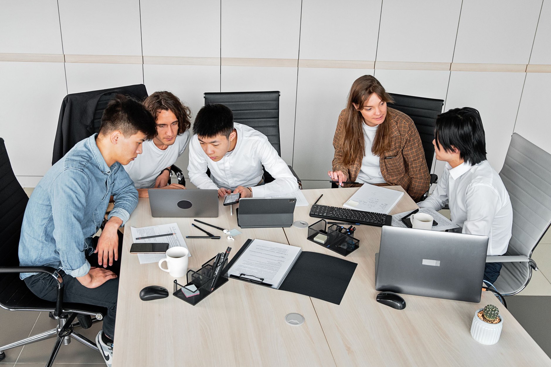 Compañeros en una mesa de oficina con portátiles, tabletas y móviles distintos