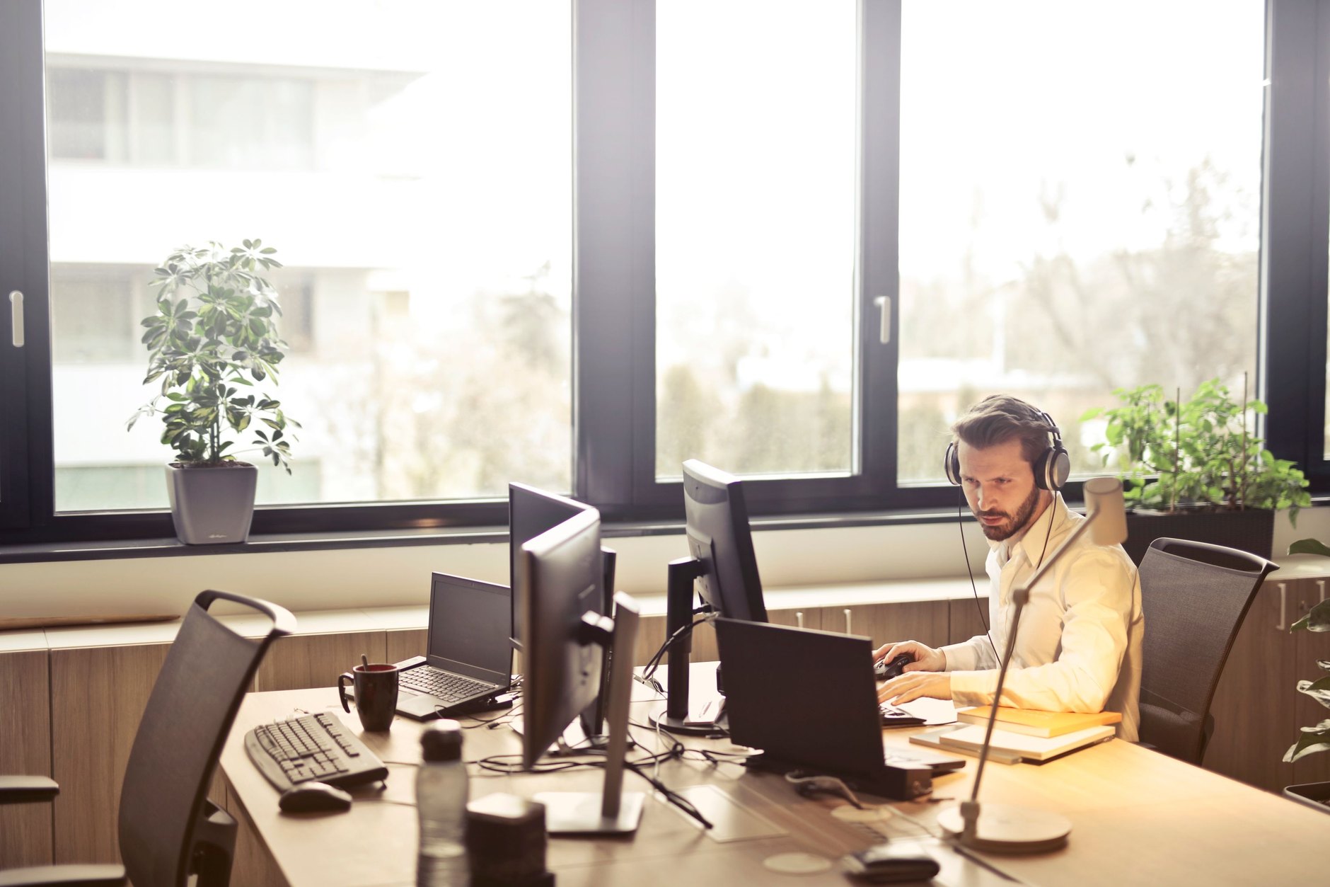 Administrador de TI en su escritorio con varias pantallas y auriculares gestionando dispositivos