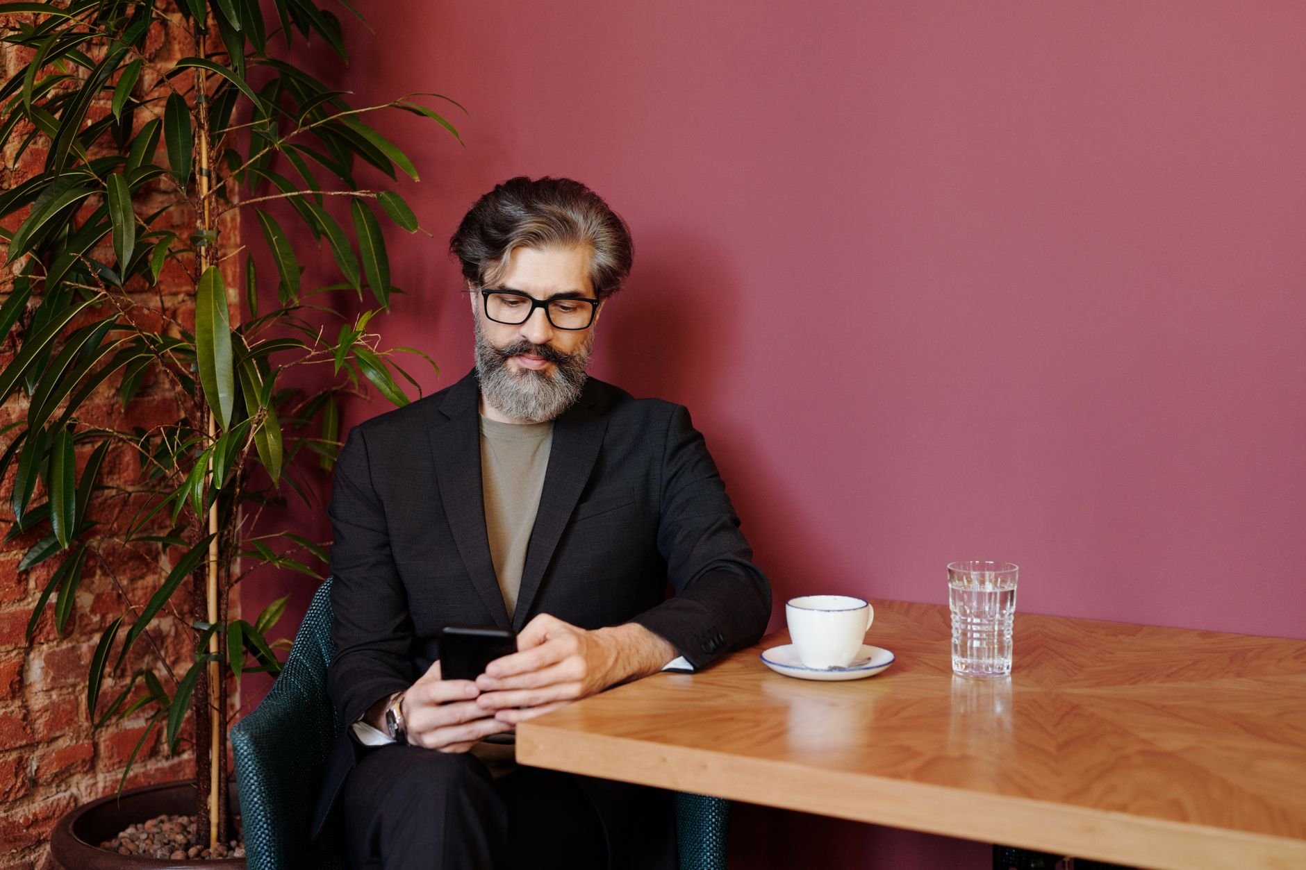 Stylish bearded man sitting in cafe using a smartphone with a cup of coffee.