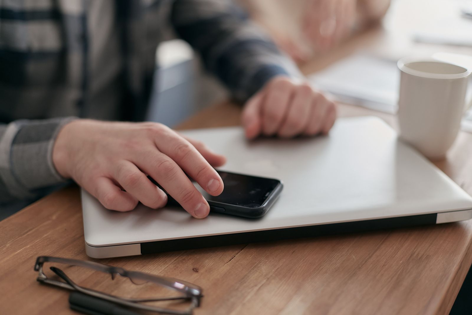 Hands on a personal smartphone resting on a closed laptop, a BYOD work setup (Mikhail Nilov, Pexels)