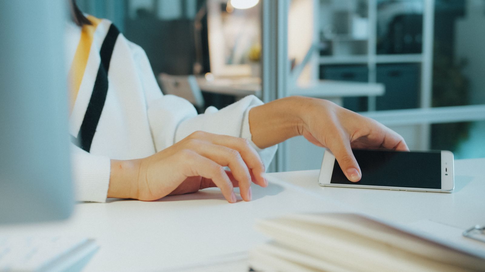 A hand holding a smartphone above a desk in an open office (Vitaly Gariev, Pexels)