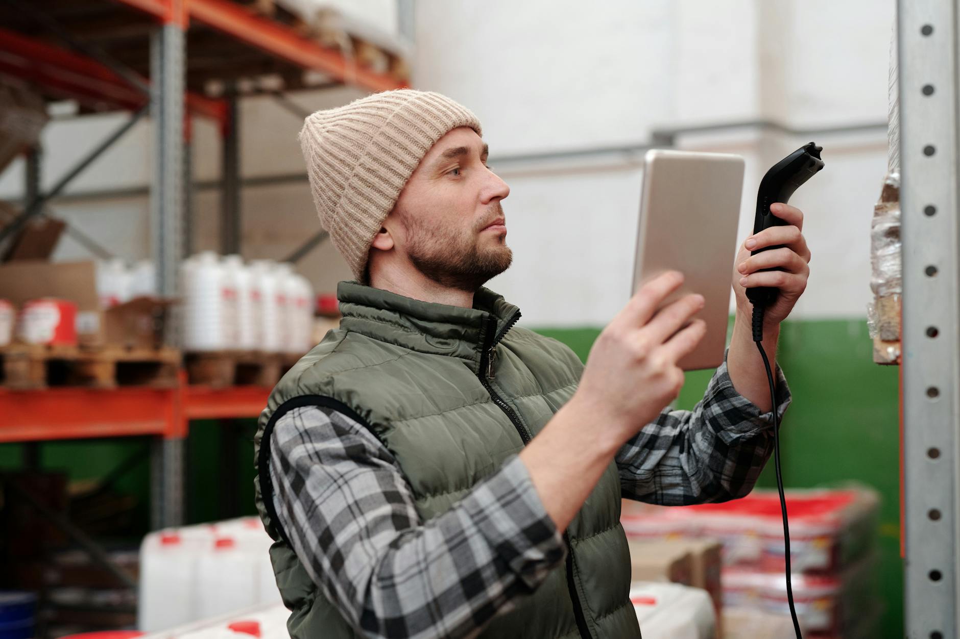 Man in beanie and vest using a scanner in a warehouse for inventory control. - Photo par Tiger Lily sur Pexels